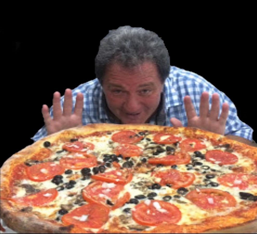 A man with gray hair joyfully displays a large pizza topped with slices of tomato, olives, and other ingredients, set against a black background.