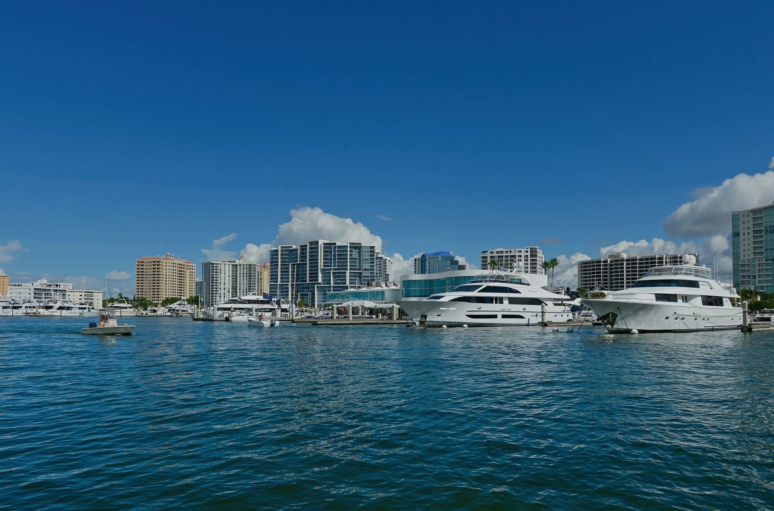 Luxury waterfront marina in Venice, FL, featuring upscale yachts and high-rise buildings against a clear blue sky.