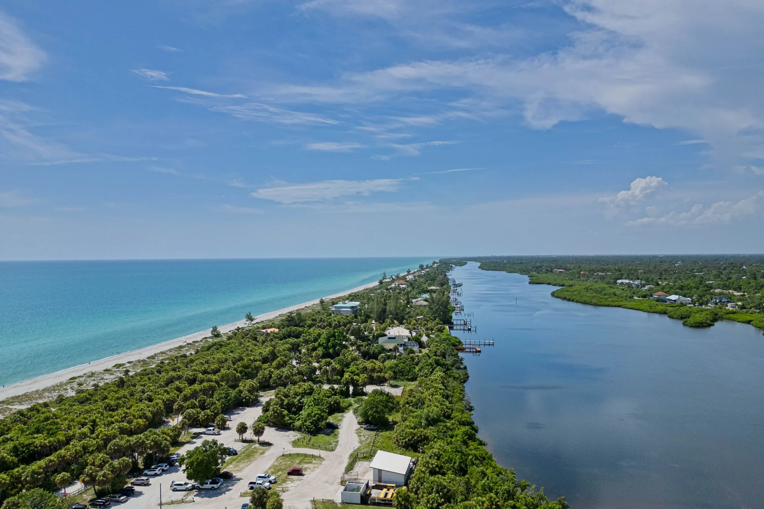 Aerial view of Venice, FL coastline with sandy beach, turquoise waters, lush greenery, and winding river, highlighting the area's natural beauty and potential for outdoor recreation.