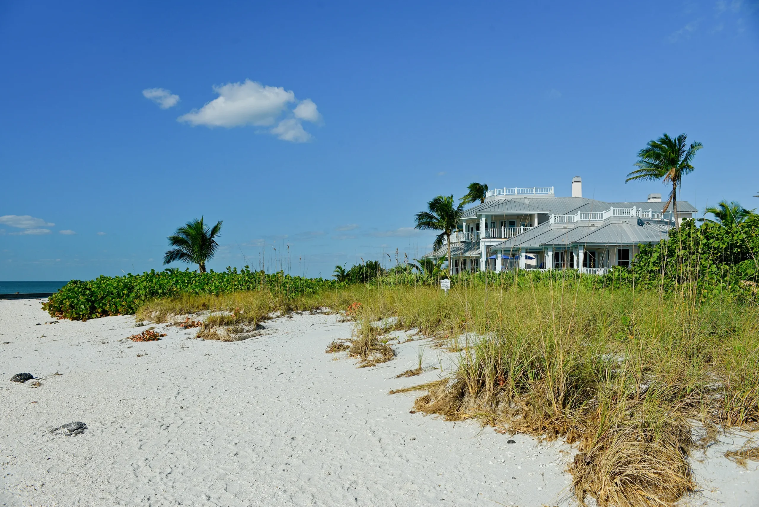 Luxury waterfront home in Venice, FL, surrounded by sandy beach and lush greenery under a clear blue sky.